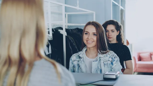 Two young women shopping and interacting with cashier in clothing store. Returns programme improvement